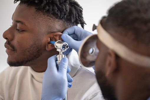 Close up of a male  doctor carefully holding the ear of his patient to establish a clearer view of the inside of his ear, to see if he requires hearing aids at a modern clinic