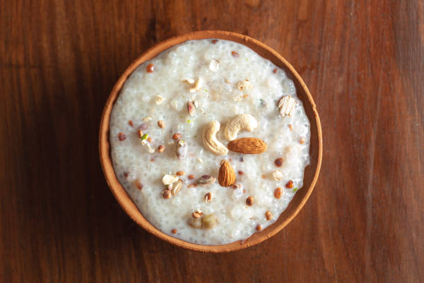 Close up of a famous Bengali dessert "Nolen Gurer Chanar Payesh" or Milk pudding of cottage cheese in an earthen pot called "Kullahad". Over wooden background. Close up of a famous Bengali dessert "Nolen Gurer Chanar Payesh" or Milk pudding of cottage cheese in an earthen pot called "Kullahad". Top-down view, wooden background. bengali sweets stock pictures, royalty-free photos & images