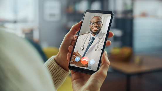 Close Up of a Female Has a Video Call with Her Female Family Doctor on Smartphone from Living Room. Ill-Feeling Woman Making a Call from Home with Physician Over the Internet.