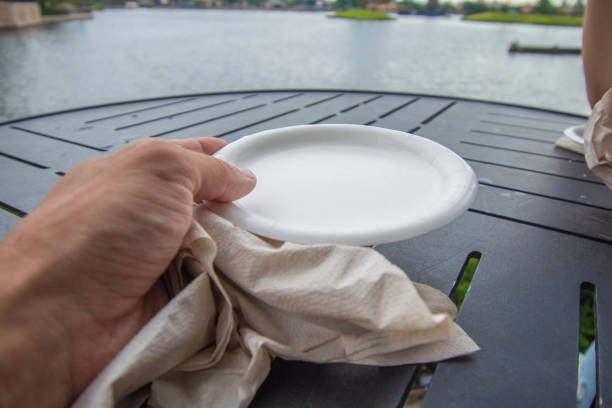 A close up of a hand holding a wrinkled napkin and an empty paper plate stock photo