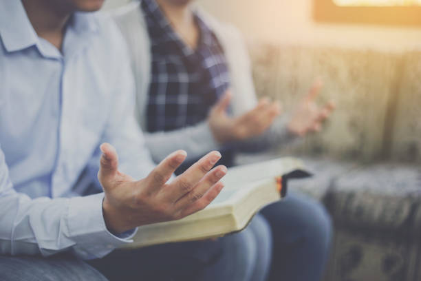 Close up of a man holding bible and raise hand up  praying to God with his friends stock photo
