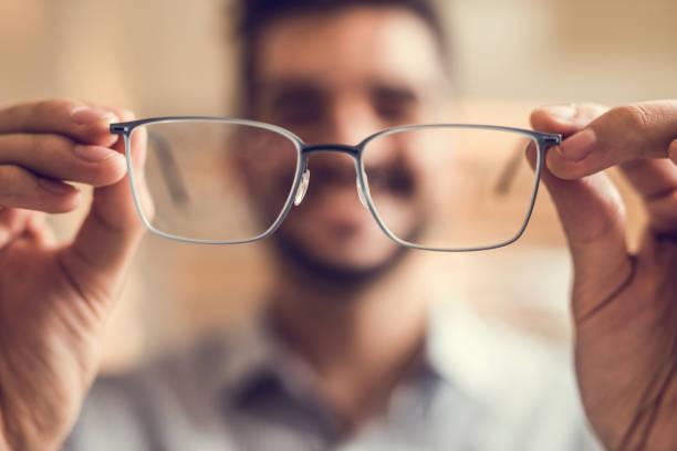 Close up of a man holding eyeglasses before trying them on. Close up of unrecognizable man trying on eyeglasses. lens optical instrument stock pictures, royalty-free photos & images
