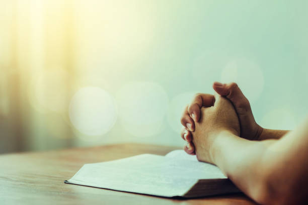 Close up of a man's hands praying on the holy  bible  on wooden table stock photo