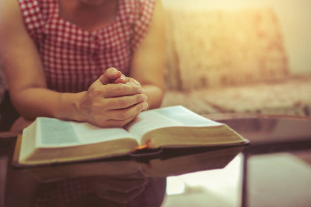 Close up of a woman hands praying on an open bible on a wooden table with window light Bokeh, Christian praise and worship, devotional concept background stock photo