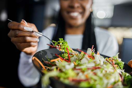 Close up of unrecognizable black woman holding a plate with multi-colored fresh salad.