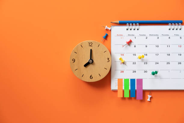 close up of alarm clock and calendar on the orange table background, planning for business meeting or travel planning concept stock photo