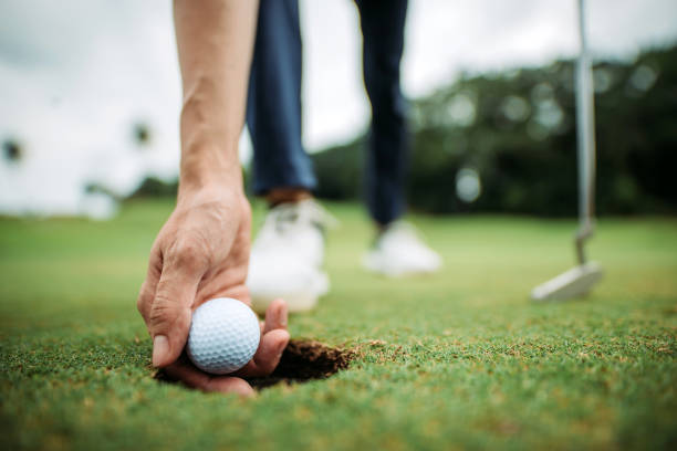 Close up of asian chinese young male golfer picking up golf ball with hand at the hole of golf course Bend over to take out the golf ball with hand golf club stock pictures, royalty-free photos & images