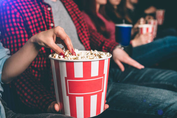 Close up of beautiful red basket with popcorn. Guy is holding it. Girl's hand is taking some popcorn from it. stock photo