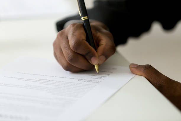 Close up of black worker signing legal documentation Close up of African American worker signing job contract, person being employed at new position, male client putting signature at document in office. Recruiting, promotion, legal documentation concept form filling stock pictures, royalty-free photos & images