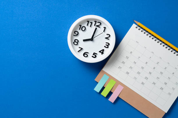 close up of calendar and alarm clock on the blue table background, planning for business meeting or travel planning concept stock photo