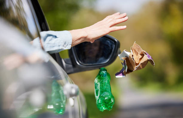 Close Up Of Driver In Car Dropping Trash Out Of Window On Country Road stock photo