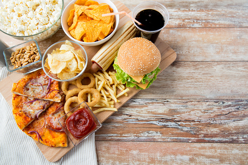 fast food, junk-food and unhealthy eating concept - close up of fast food snacks and coca cola drink on wooden table