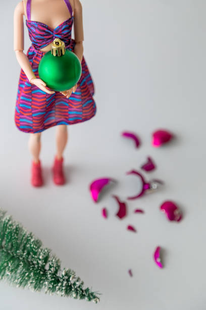 Close up of female doll holding Christmas bauble next to broken one on the floor and knocked down fir tree minimal creative holiday concept. Top view of fashionable doll with Christmas decoration ball. Pink shattered bauble and christmas tree on the floor. broken doll 1 stock pictures, royalty-free photos & images