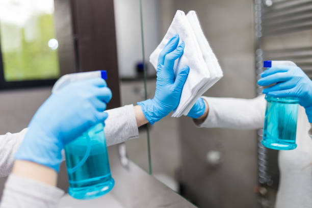 Close up of female hands with medical gloves polishing mirror with rag and using disinfectant spray. Housekeeping and cleaning service. stock photo