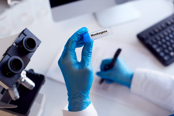 close up of female lab worker wearing ppe researching monkeypox with microscope - monkeypox stockfoto's en -beelden
