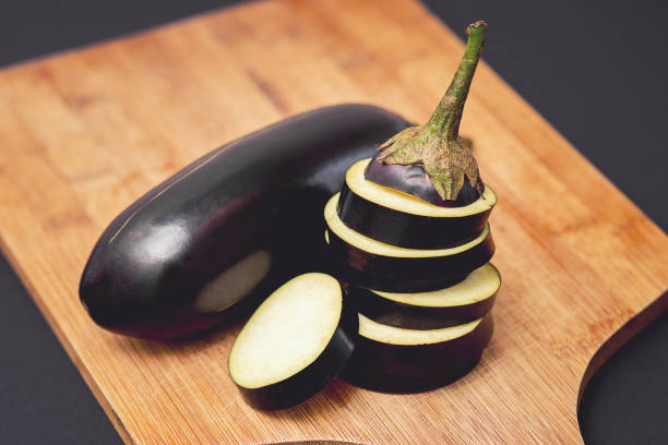 Close up of fresh healthy whole and sliced eggplants. Close up of fresh healthy whole and sliced eggplants on a wooden cutting board on the black background. eggplant stock pictures, royalty-free photos & images