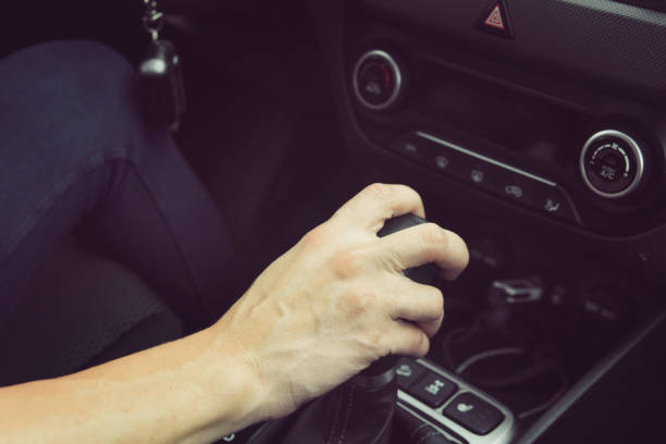 Close up of girl driving car moving transmission shift gear. Concept of female driving car. Using vehicle with modern automatic gearbox. Moment of shifting gear. Pushing gearstick to change speed. stock photo