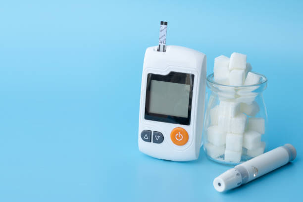 close up of Glucose meter, lancet and jar of sugar cubes on blue background. stock photo