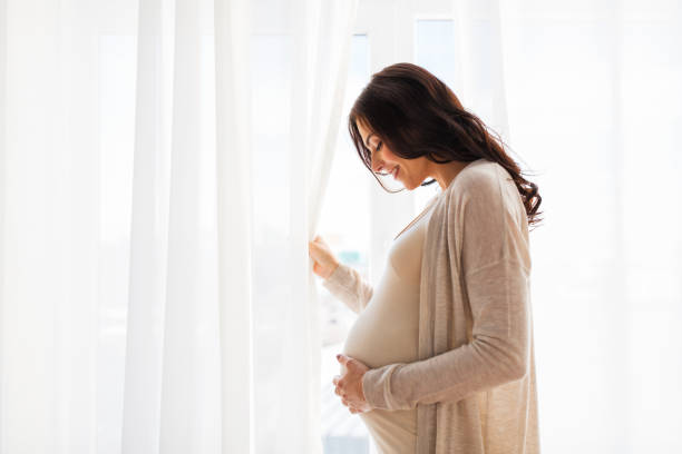 close up of happy pregnant woman with big belly pregnancy, motherhood, people and expectation concept - close up of happy pregnant woman with big belly at window pregnant stock pictures, royalty-free photos & images