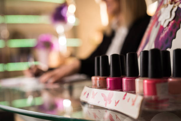 Close up of large group of multi-colored nail polish. Close up of group of nail polish in nail salon with a person in the background. nail salon stock pictures, royalty-free photos & images