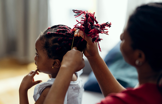 Beautiful little girl getting her hair twisted by her mom at home