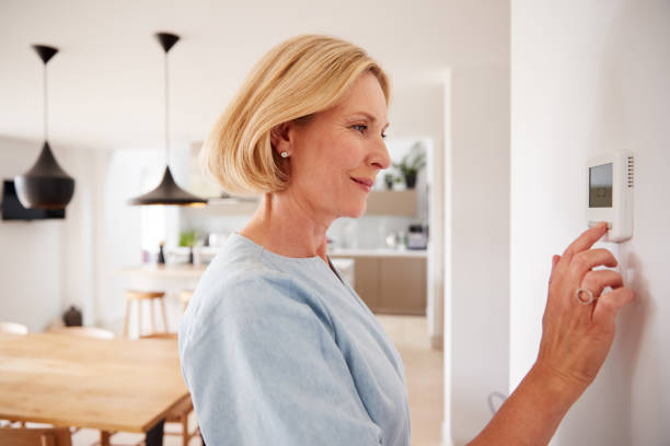 Close Up Of Mature Woman Adjusting Central Heating Temperature At Home On Thermostat Close Up Of Mature Woman Adjusting Central Heating Temperature At Home On Thermostat thermostat stock pictures, royalty-free photos & images