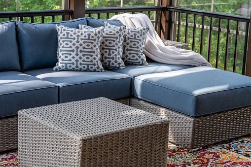 Close up of patio furniture in modern screened porch, summertime woods in the background.