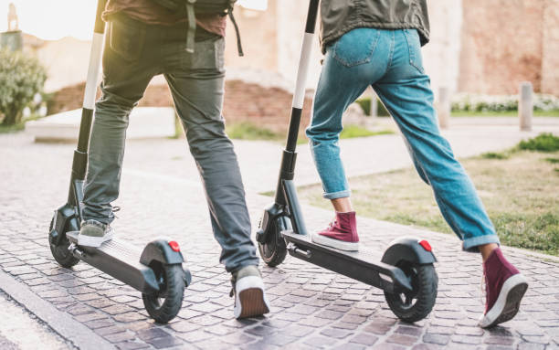 Close up of people couple using electric scooter in city park - Millenial students riding new modern ecological mean of transport - Green eco energy concept with zero emission - Warm sunshine filter stock photo