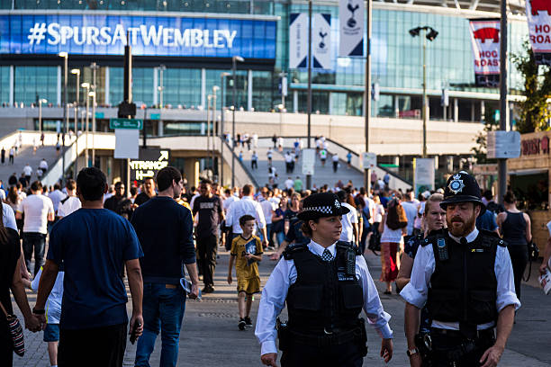 Close up of police and supporters outside Wembley Stadium, London London, UK - September 14, 2016: close up image of two police officers, a man and a woman, outside Wembley stadium in London, UK, prior to the Champions League match between Tottenham Hotspur FC and AS Monaco. They are surrounded by fans of Tottenham Hotspur, and the modern glassy facade of the stadium looms behind them in the background. Tottenham Hotspur stock pictures, royalty-free photos & images