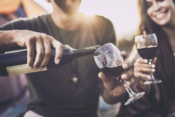 Close up of pouring red wine into a glass outdoors. Close up of a couple drinking wine outdoors while man is pouring it into a glass. bottle of wine stock pictures, royalty-free photos & images