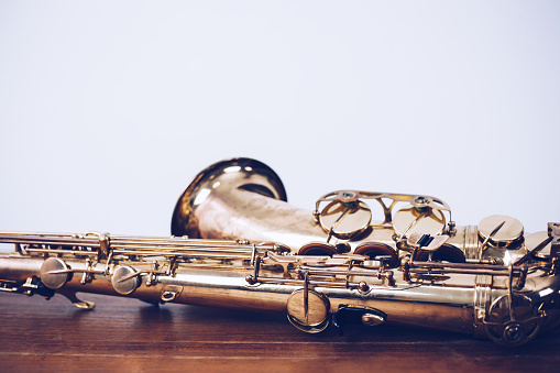 close up of  saxophone on wooden table with white wall texture background, music background with copy space.