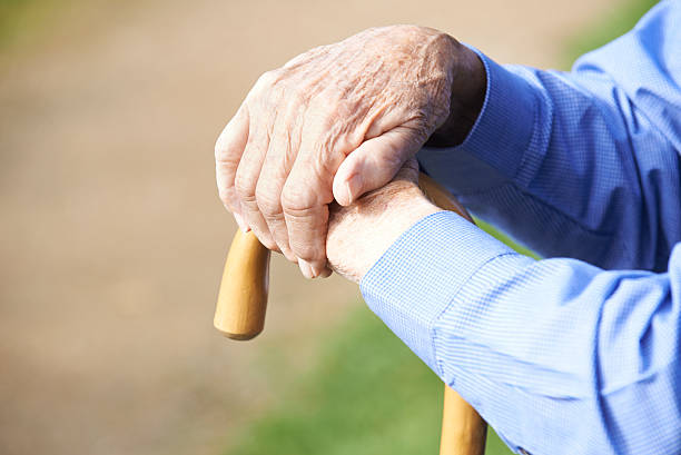 Close Up Of Senior Man's Hands Resting On Walking Stick stock photo