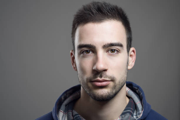 Close up of serious young unshaven man wearing hoodie Close up of serious young unshaven man wearing hoodie looking at camera brown eyes stock pictures, royalty-free photos & images