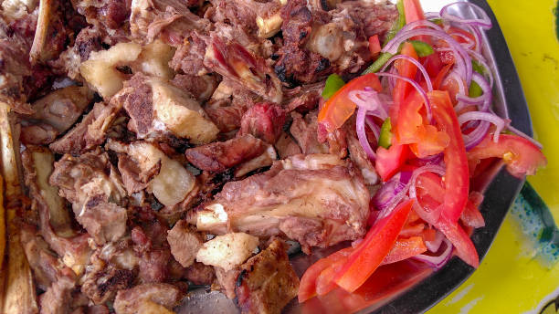 Close up of sharing platter of a traditional Kenyan dish, Nyama choma with accompaniment of kachumbari salad, of tomatoes and red onion. stock photo