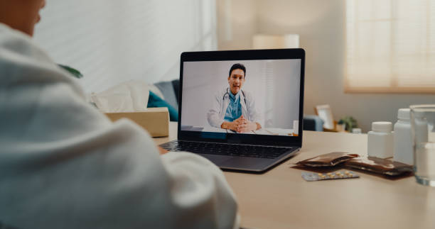 Close up of sick young Asian woman using laptop talk to doctor in living room at home. Close up of sick young Asian woman using laptop talk to doctor in living room at home. Telemedicine and Healthcare concept. doctor of physio therapy online stock pictures, royalty-free photos & images