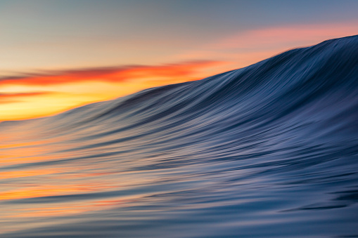 Close up of smooth wave forming on the beach with warm sunrise, California