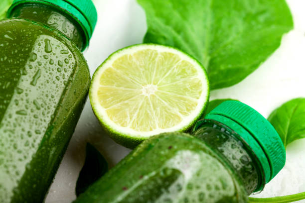 Close up of the lime slice lying between the bottles of green beverage on white backfround. The concept of creating a refreshing drink stock photo