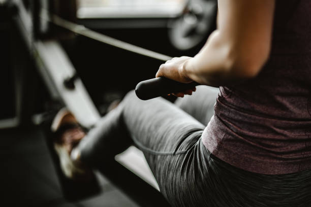 primer plano de mujer irreconocible haciendo ejercicio en una máquina de remo en un gimnasio. - centro de bienestar fotografías e imágenes de stock