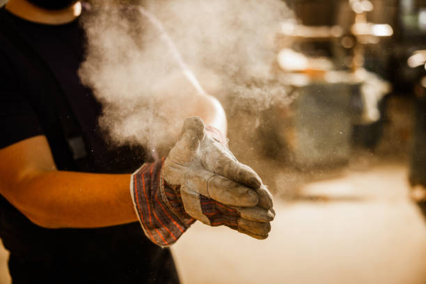 Close up of unrecognizable manual worker cleaning sawdust from his protective gloves in a workshop.