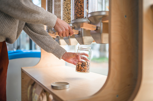 Close up of a dispenser filled with nuts in a sustainable plastic free shop. Hispanic woman refilling her jar with nuts.