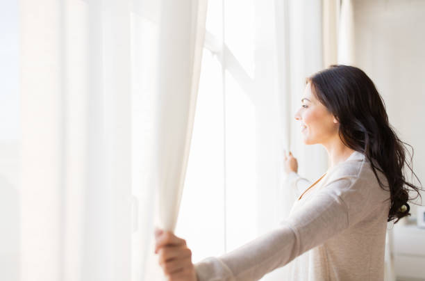 close up of woman opening window curtains people and hope concept - close up of happy woman opening window curtains looking through window stock pictures, royalty-free photos & images