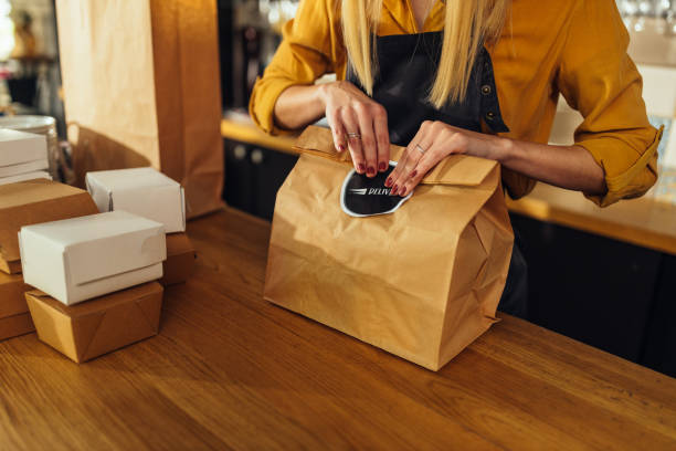 Close up of woman packing food for delivery Close up of young woman packing food in paper bags and preparing them for delivery take out food stock pictures, royalty-free photos & images