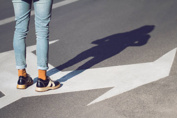 close up of woman shoes standing on the street side view close up of a young woman wearing black shoes and blue jeans standing on a street with arrow signs pointing in different directions concept for life choices guide occupation stock pictures, royalty-free photos & images