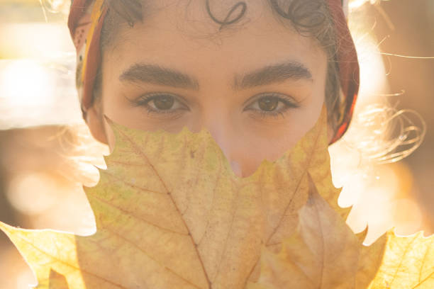 Close up of woman's face while covering mouth with autumn leaf stock photo