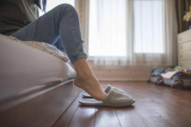 Close up of woman's feets while sitting on bed and putting on slippers stock photo