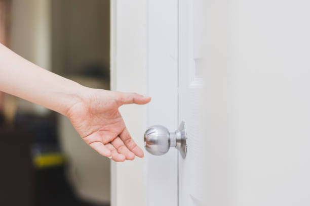 close up of woman’s hand reaching to door knob, opening the door stock photo