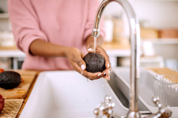Close up of woman's hands washes a avocado under water in a domestic kitchen stock photo