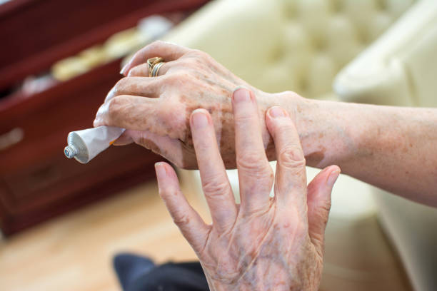 Close up of wrinkled hands applying cream at home. stock photo