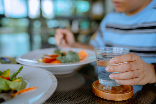 cận cảnh người phụ nữ trẻ châu á uống một ly nước và ăn thức ăn thuần chay trong khi ăn trong nhà hàng - slimming lunch hình ảnh sẵn có, bức ảnh & hình ảnh trả phí bản quyền một lần