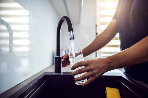 Close up of young man pouring fresh water from kitchen sink. Home interior. Close up of young man pouring fresh water from kitchen sink. Home interior. drinking water photos stock pictures, royalty-free photos & images